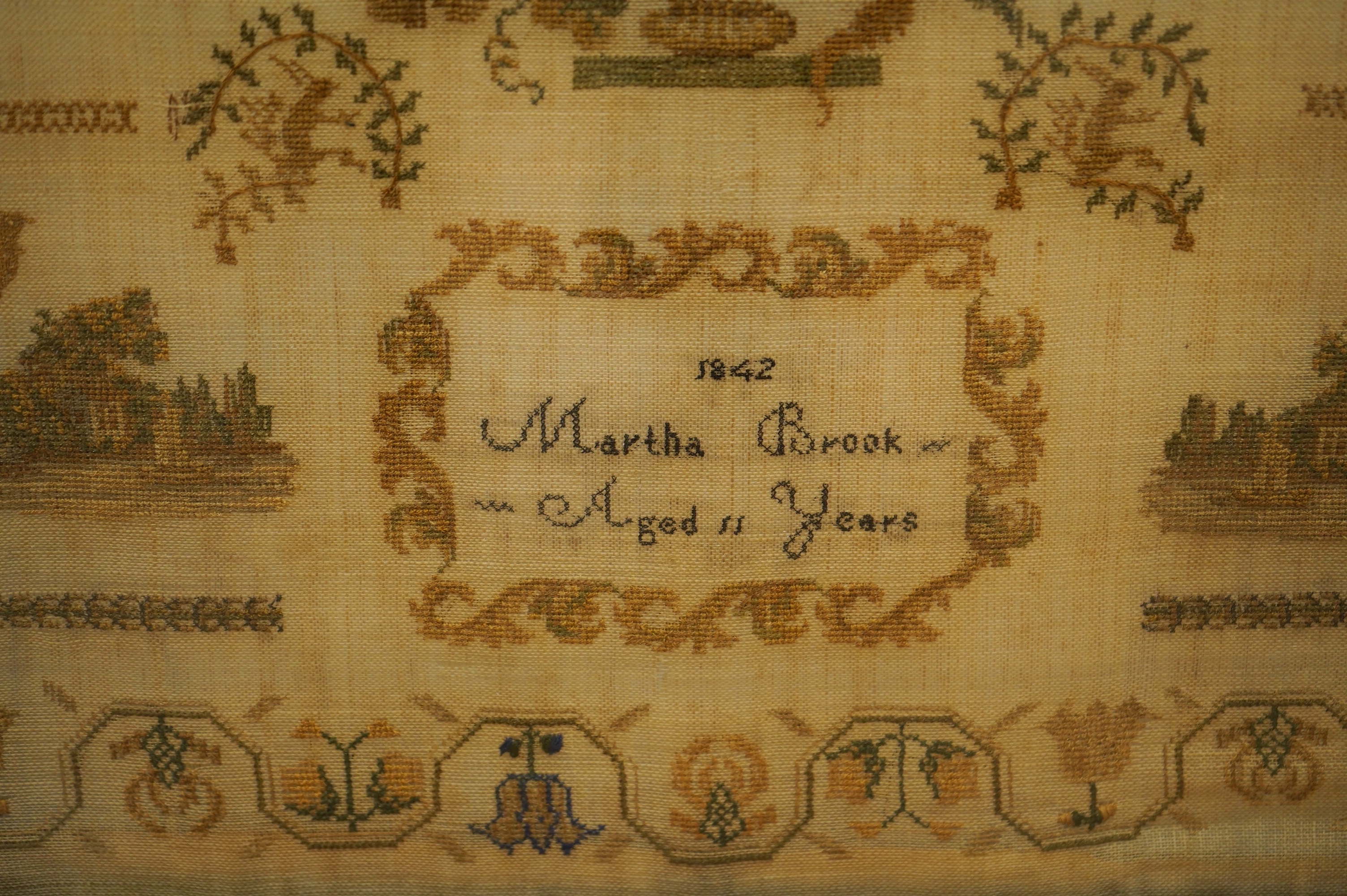 A rosewood framed sampler, dated 1842, by Martha Brook, aged 11years, worked above with large motifs of flower baskets and a bird, a vase of flowers beneath, surrounded by crowns, butterflies and chicks above two small c